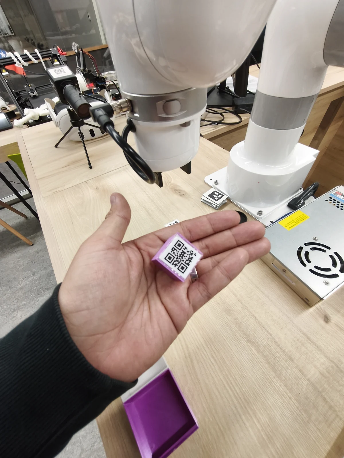 Detalle de una pieza morada con etiqueta QR sostenida frente al brazo robótico